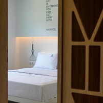 A minimalist bedroom with a bed, a wall-mounted light fixture, and a quote by Warhol.