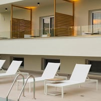 Un espacio lounge moderno al aire libre con sillones blancos y una piscina.