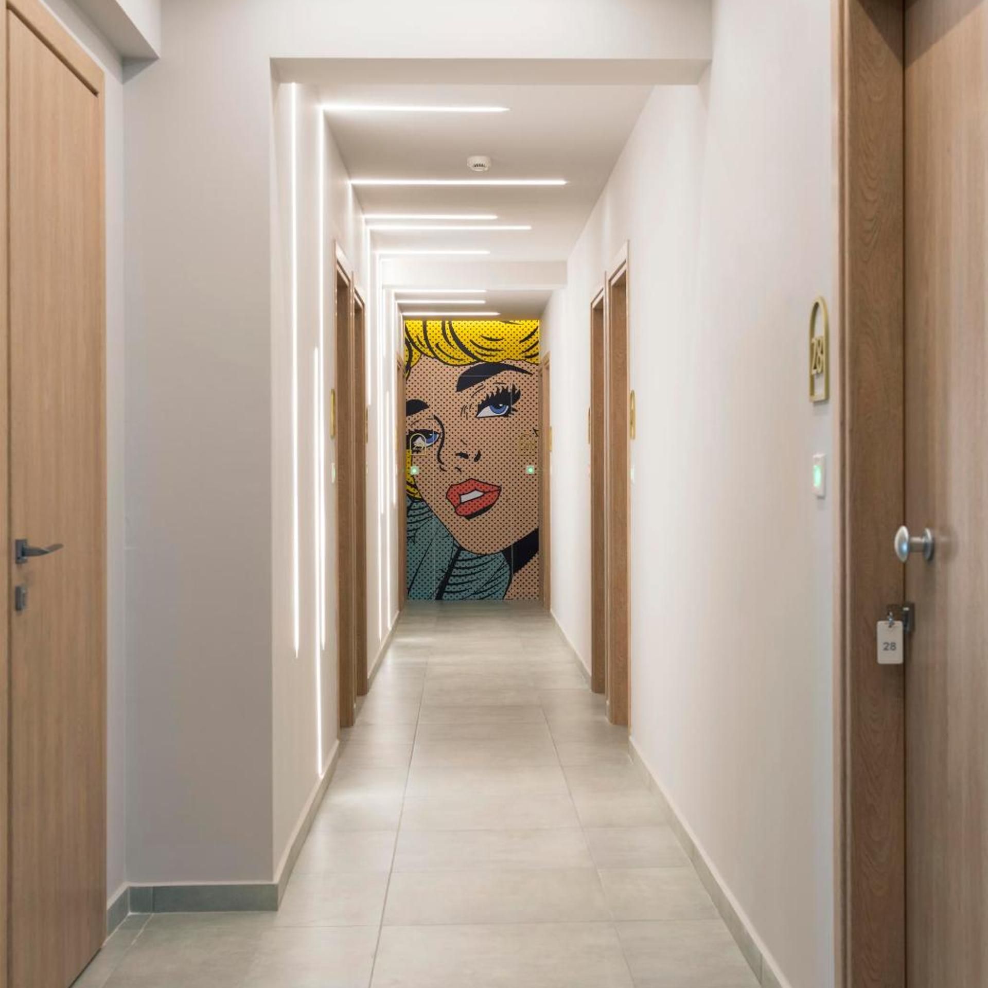 Un pasillo de hotel con puertas de madera, suelo de baldosas y un mural de estilo pop en la pared.