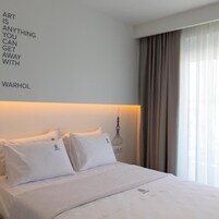 Una habitación de hotel con cama, almohadas, una pared con una cita y una ventana con cortinas.