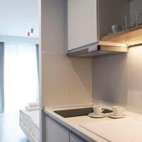 A modern kitchen with white cabinetry, a stainless steel range hood, and a countertop with two white cups and saucers.