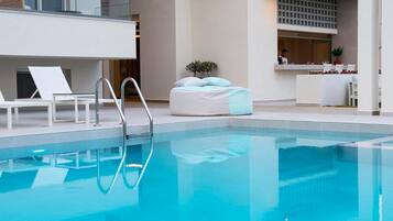 Zona de piscina moderna de hotel con piscina cristalina, sillas de descanso y un mostrador de recepción.