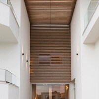 A modern interior with a slatted ceiling design, a glass door entrance, and a white wall.