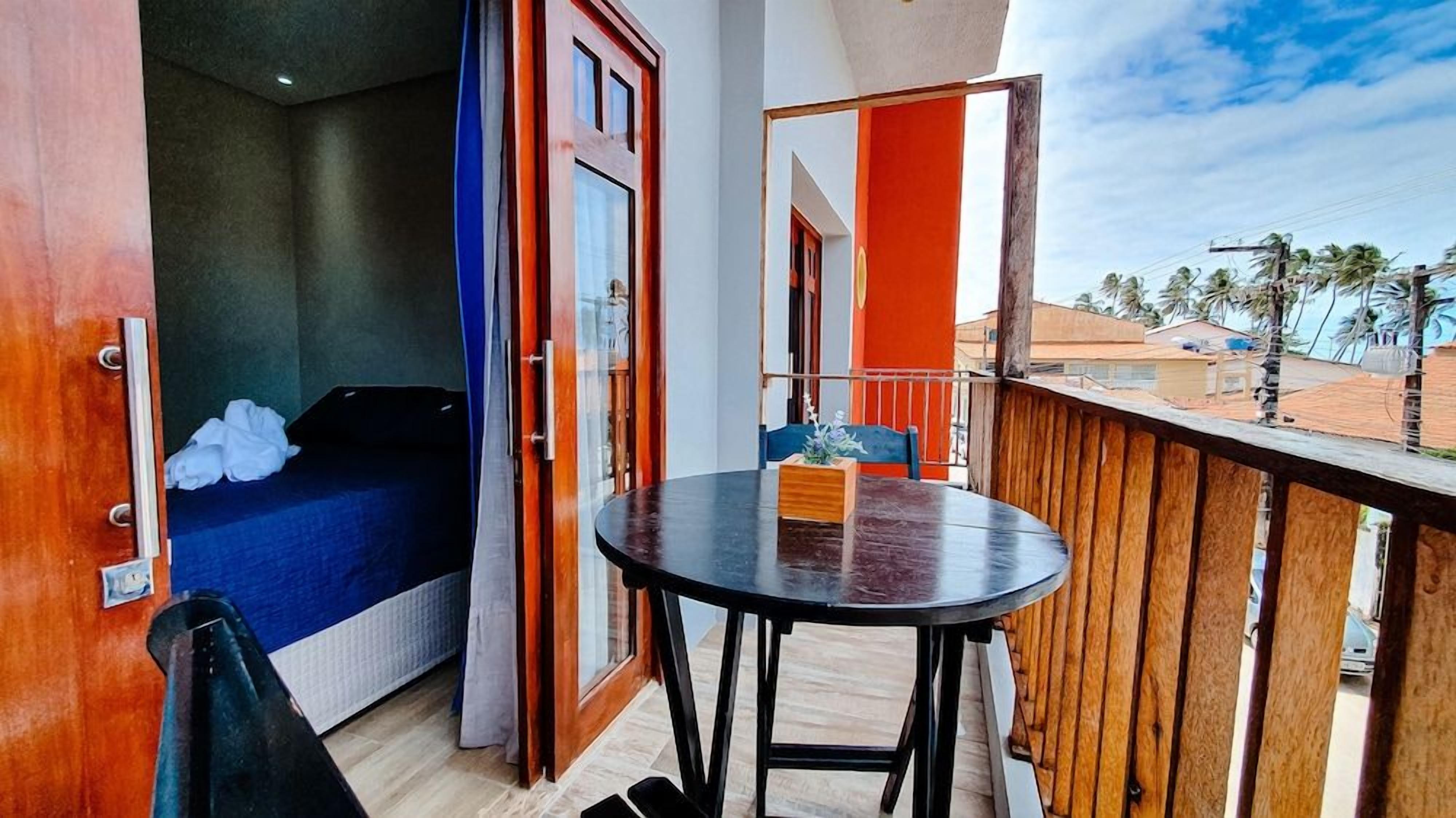 A balcony with a wooden railing, a small table with a vase, and a bed with a blue cover.