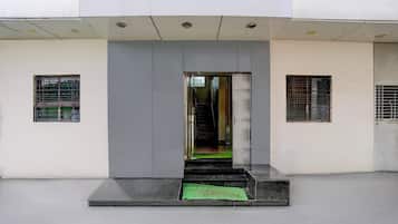 Entrada de un edificio con una puerta gris, unos escalones bajos y dos ventanas con barrotes.