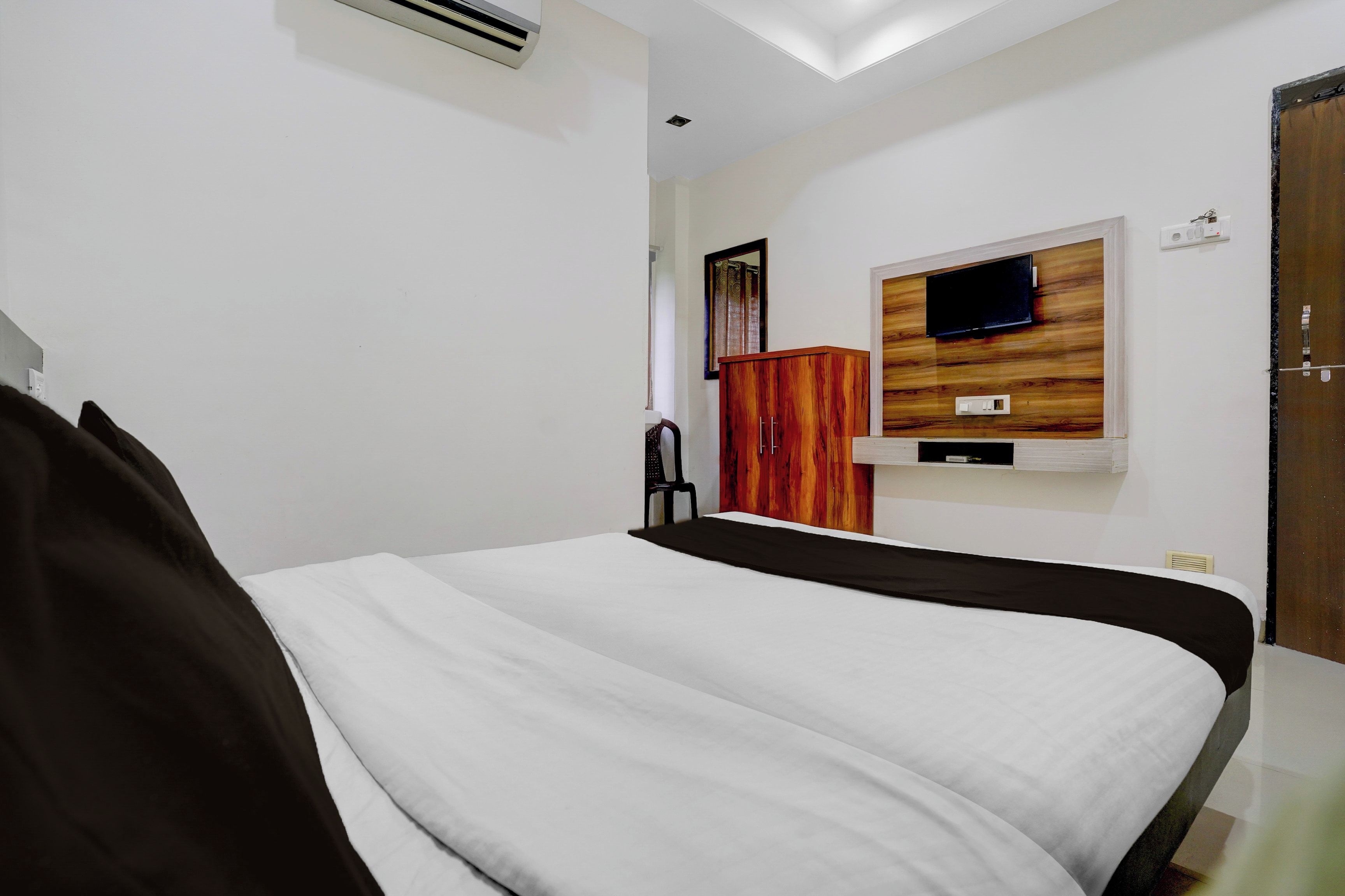 A bedroom with a bed, a wardrobe, a television mounted on the wall, and an air conditioning unit.