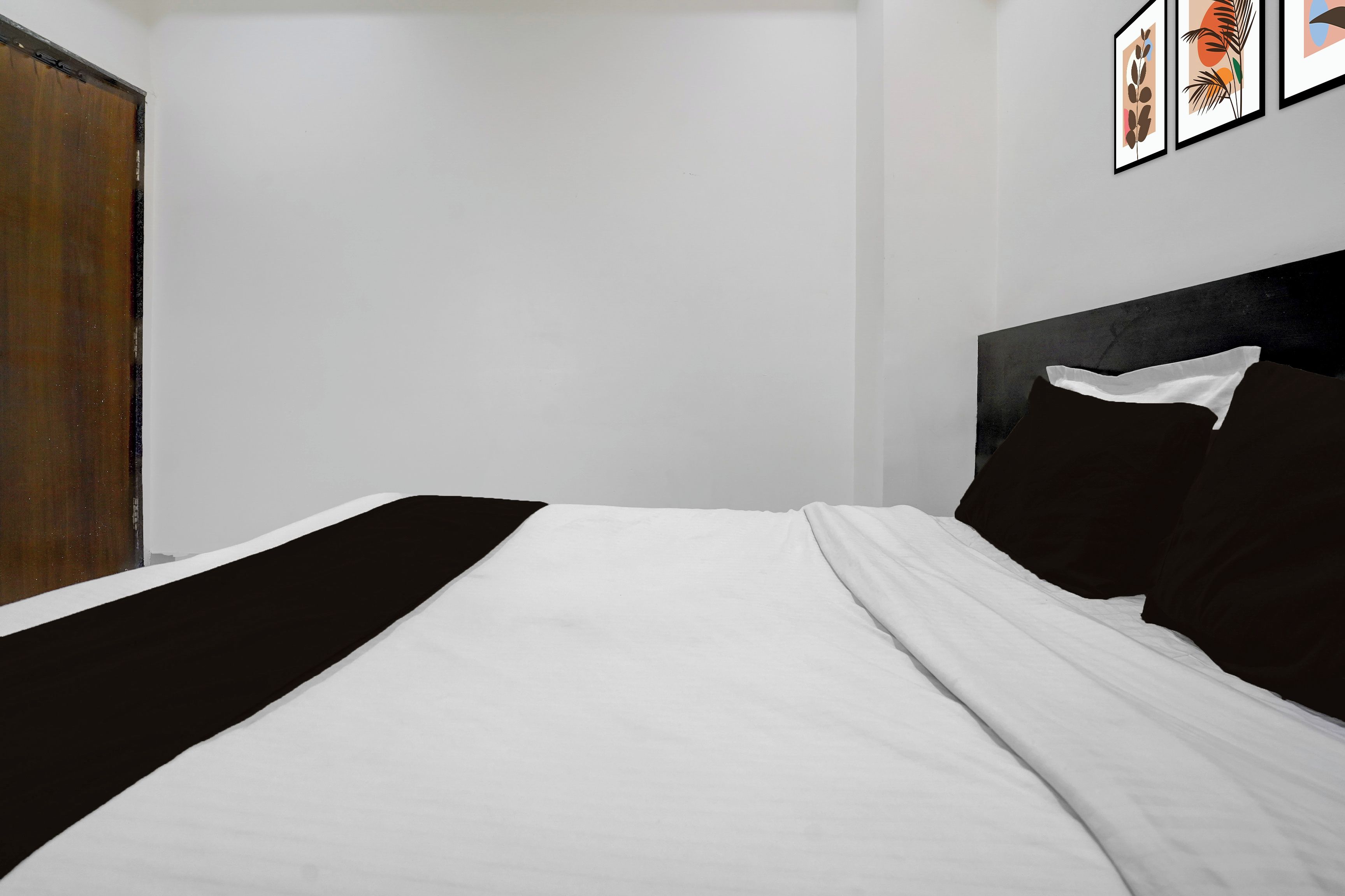 Un dormitorio con cama, una puerta de madera y cuadros en la pared.