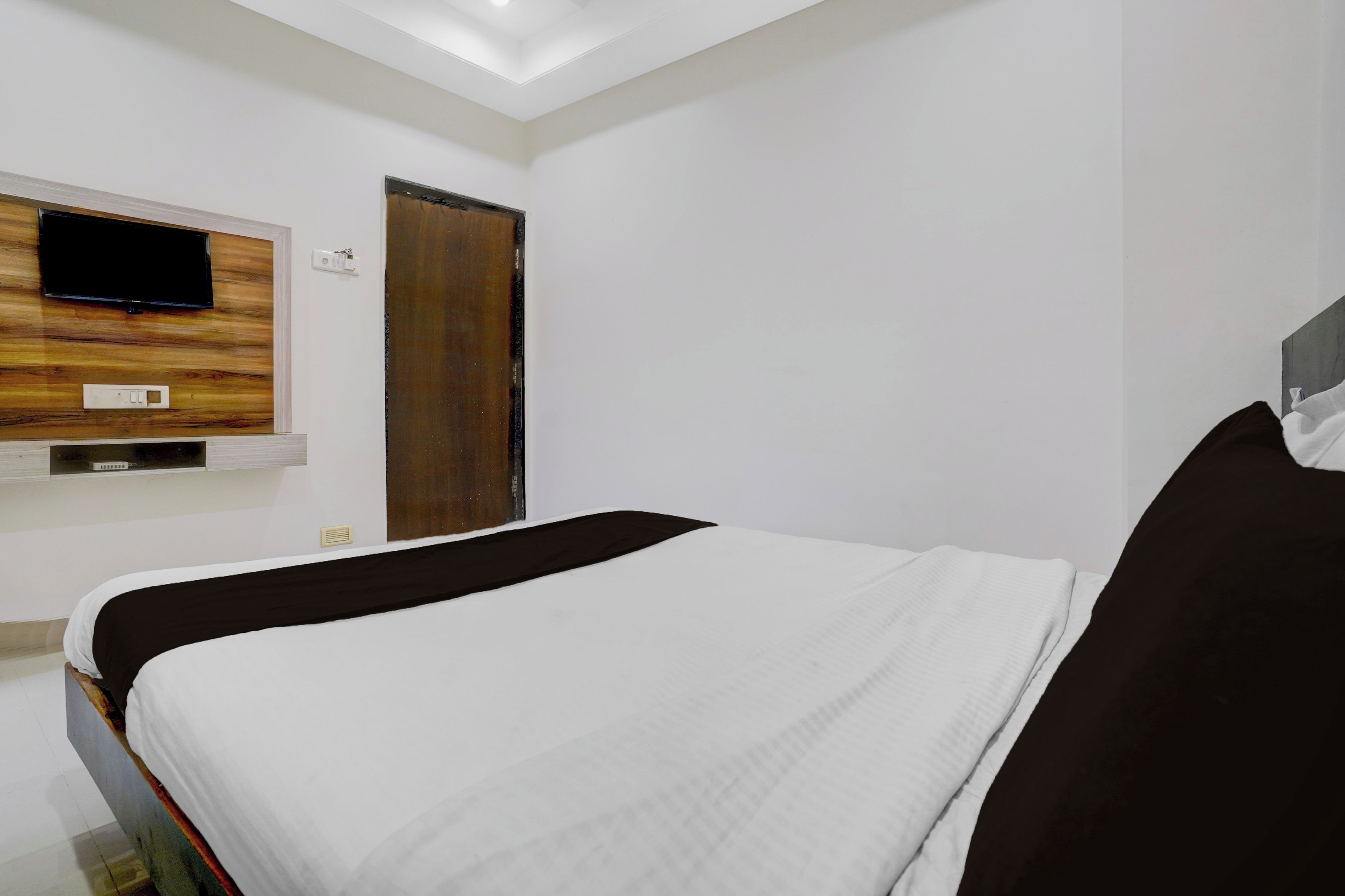 A hotel room with a bed, a television mounted on a wooden panel, a door, and a window.
