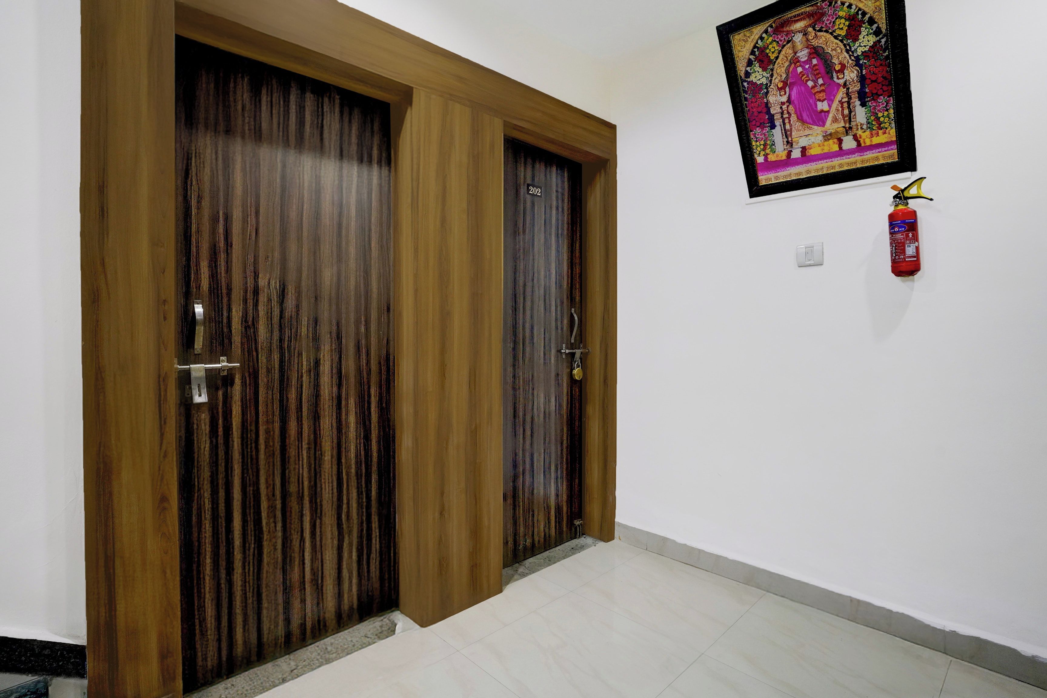 A hallway with two wooden doors, a fire extinguisher mounted on the wall, and a framed picture above the right door.