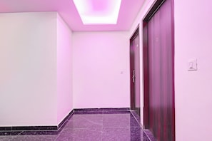 A hallway with a pink wall, a dark marble floor, and a closed wooden door. - Collection O Palam Metro Station (New Delhi)