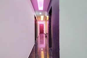 Un pasillo moderno con piso de mármol, una puerta roja al final e iluminación en el techo.