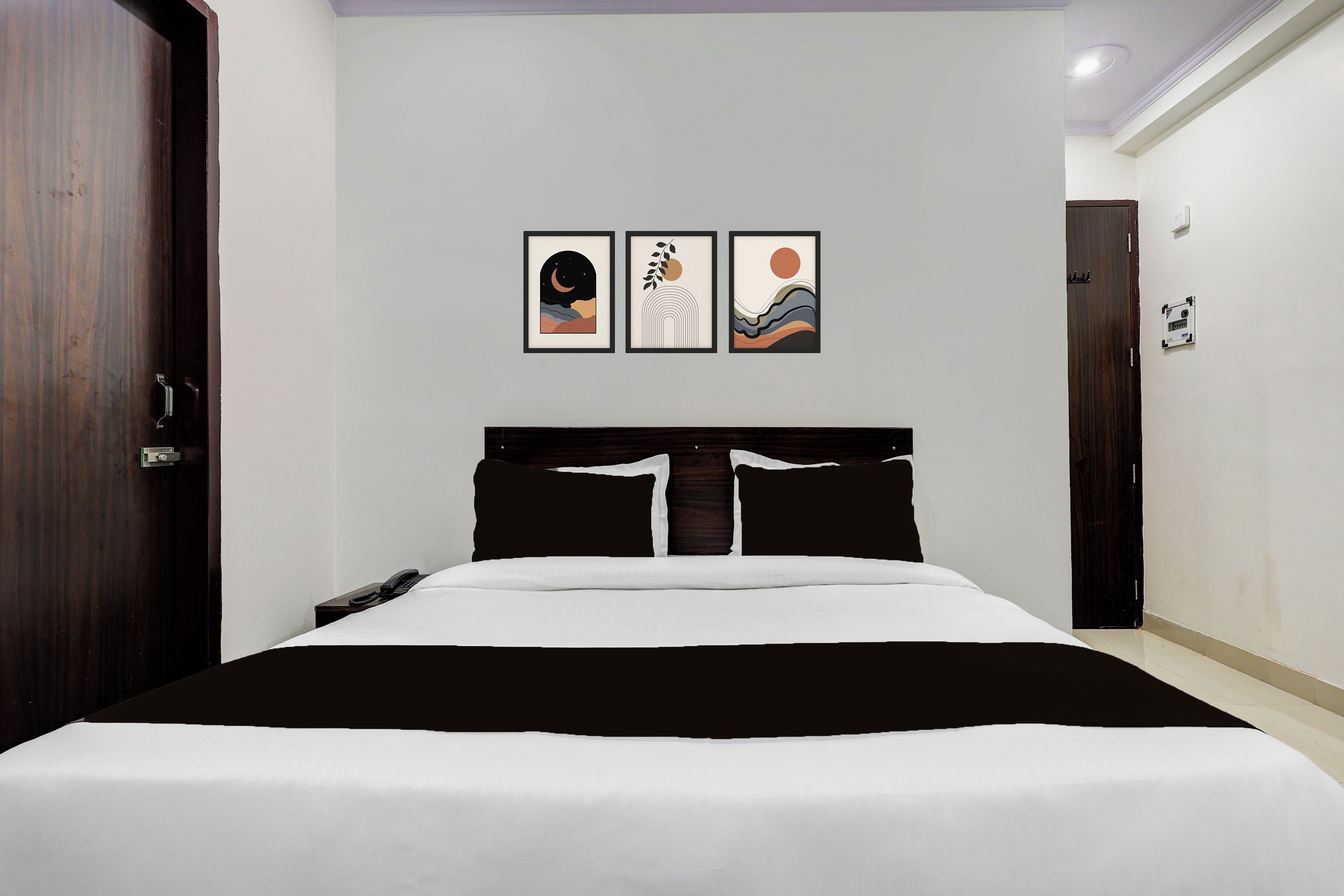 Una camera d'albergo con un letto grande, un comodino, un telefono fissato al muro e tre opere d'arte incorniciate sopra il letto.