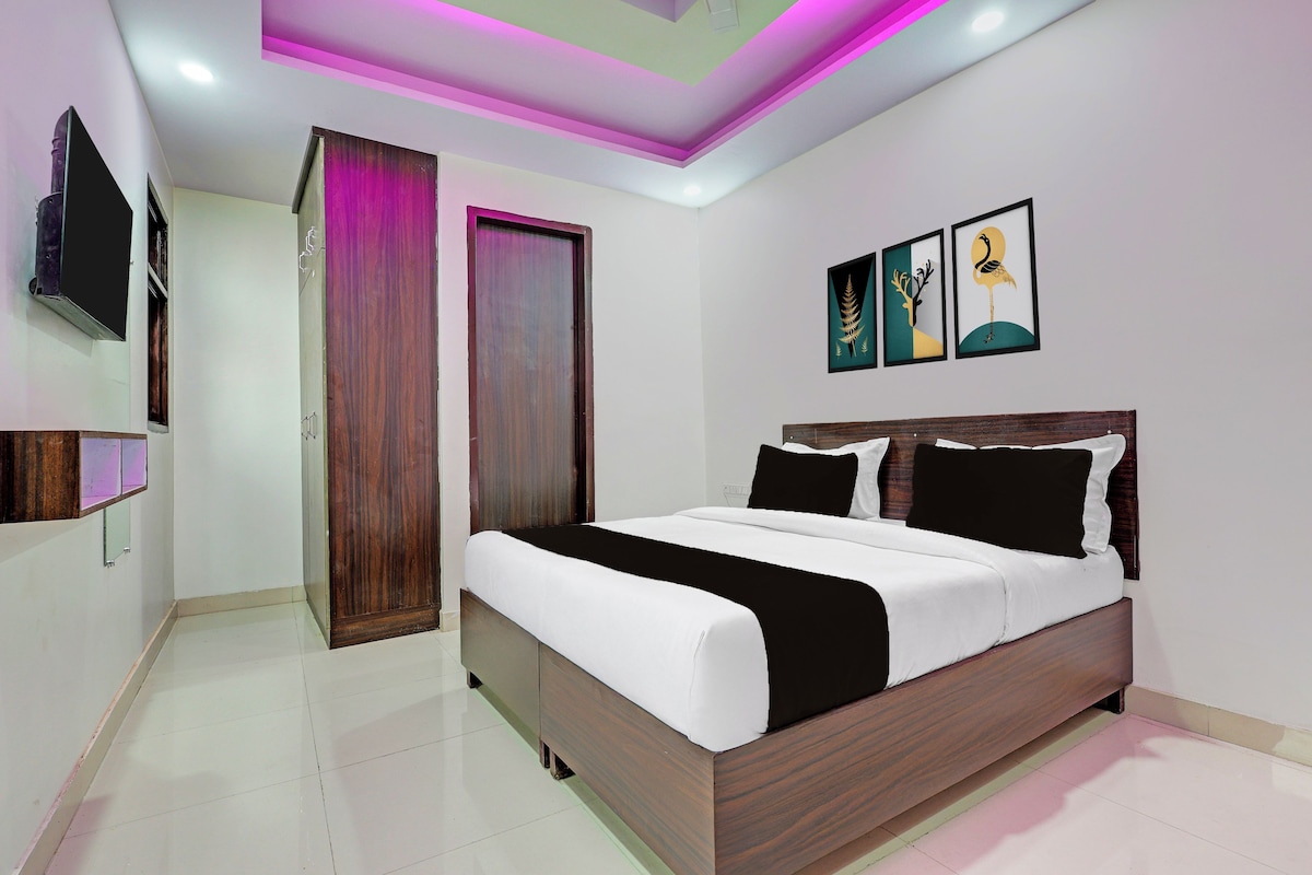 A modern bedroom with a large bed, a flat-screen TV mounted on the wall, and artwork above the bed.