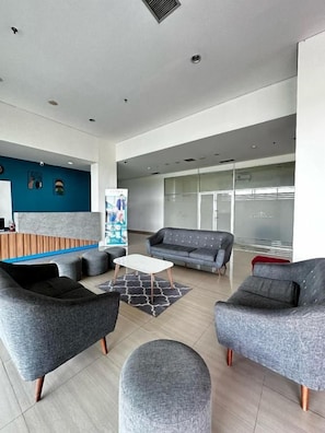 A modern lobby with grey sofas, a white coffee table, and a blue accent wall. - Izi Cozi Jababeka Enviro (Cikarang)