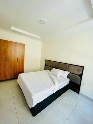 A bedroom with a bed, a wardrobe, and a ceiling light. - Convenient 2BR apartment near kigali airport (Kigali)