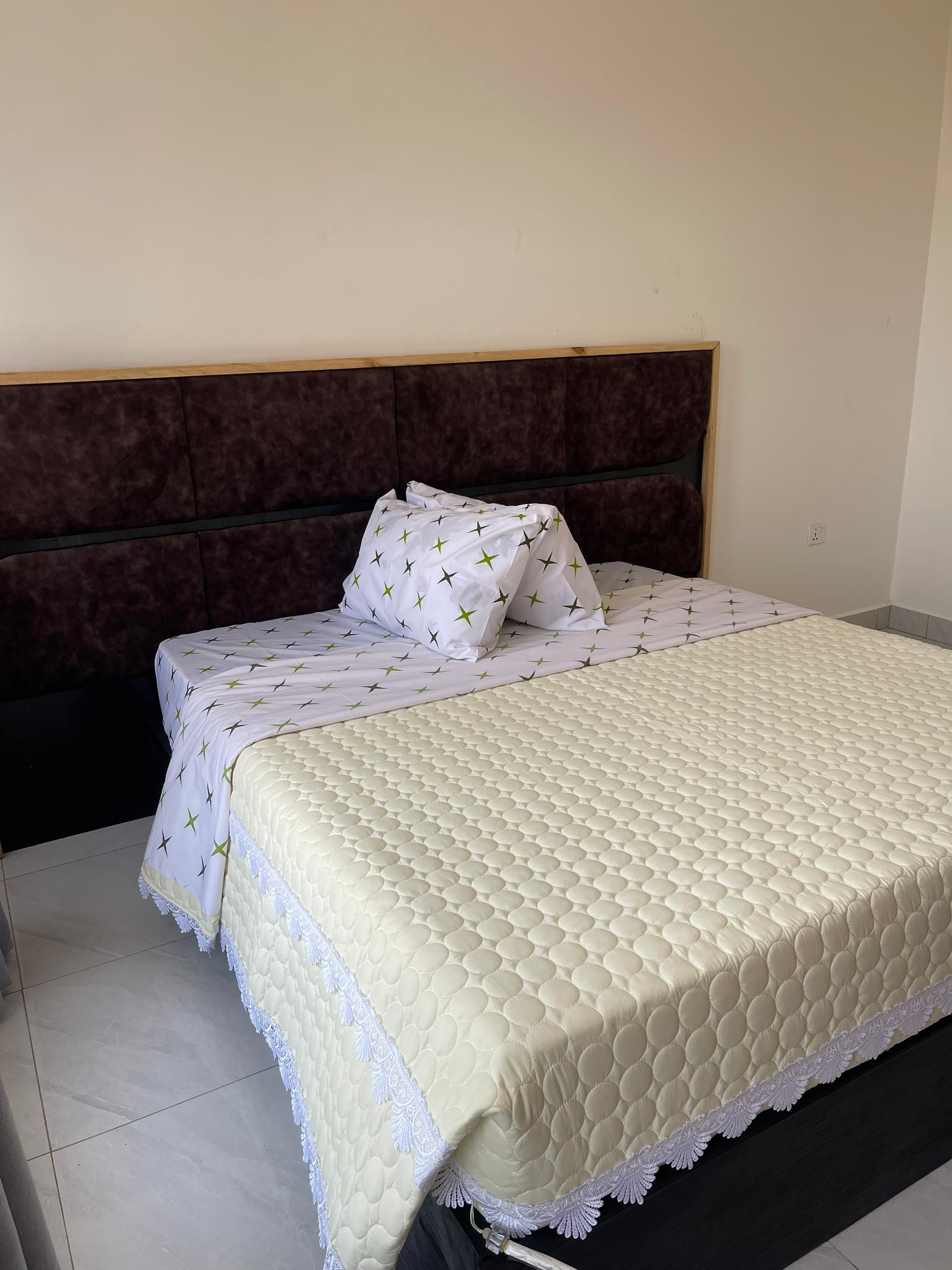 A neatly made bed with a quilted headboard and a white bedspread with a green pattern.