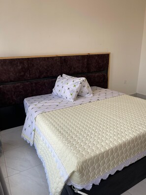 A neatly made bed with a quilted headboard and a white bedspread with a green pattern. - Convenient 2BR apartment near kigali airport (Kigali)