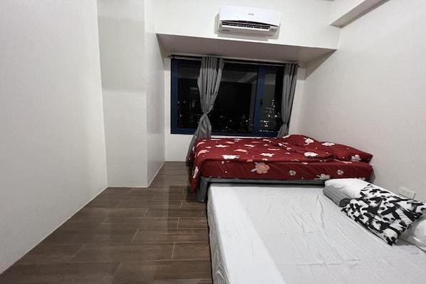 Un dormitori amb un llit, una finestra amb cortines, un aparell d'aire condicionat i vista a la ciutat.
