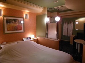 A hotel room with a bed, a mirror with lights, a painting, and a bathroom with a towel rack.