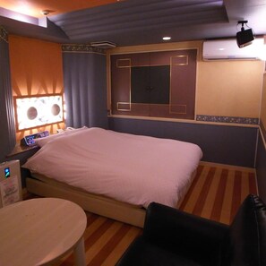 A hotel room with a bed, bedside table, lamp, and a wall-mounted air conditioning unit. - Hotel K Village (Tokorozawa)