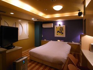A hotel room with a bed, a desk, a television, and an air conditioning unit.
