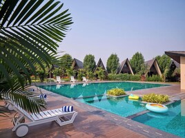 A swimming pool with lounge chairs and umbrellas, surrounded by palm trees and a clear sky.