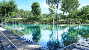 Piscina límpida com borda azulejada, rodeada por vegetação exuberante e árvores.