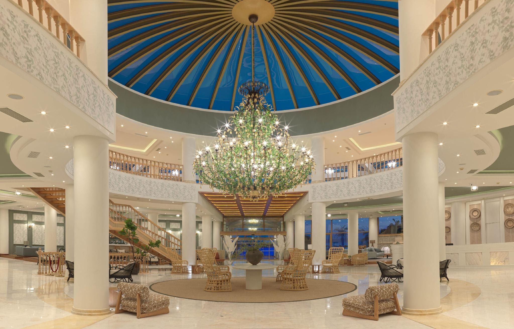 A spacious lobby with a central chandelier, multiple seating areas, and a grand staircase.