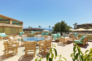 An outdoor seating area with wicker furniture and a glass table, overlooking a clear sky and distant mountains.