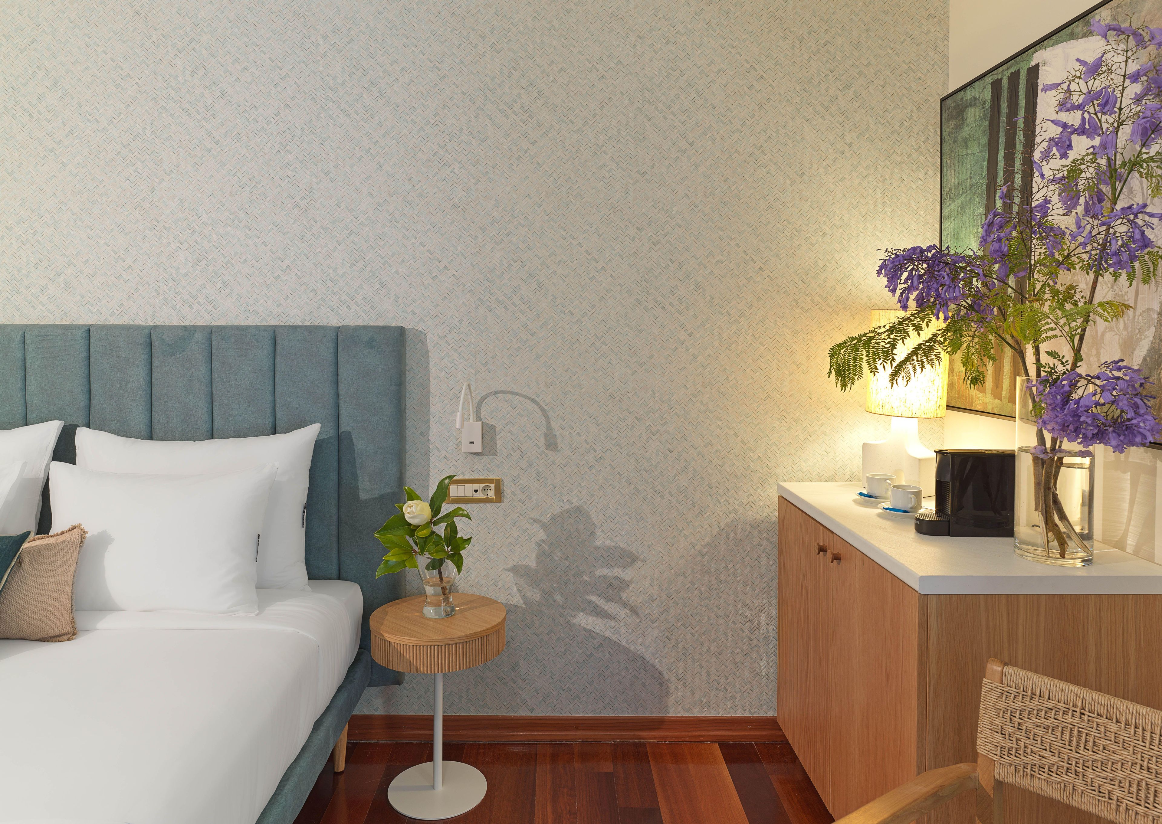 A hotel room with a bed, bedside table, lamp, and a wall-mounted power outlet.