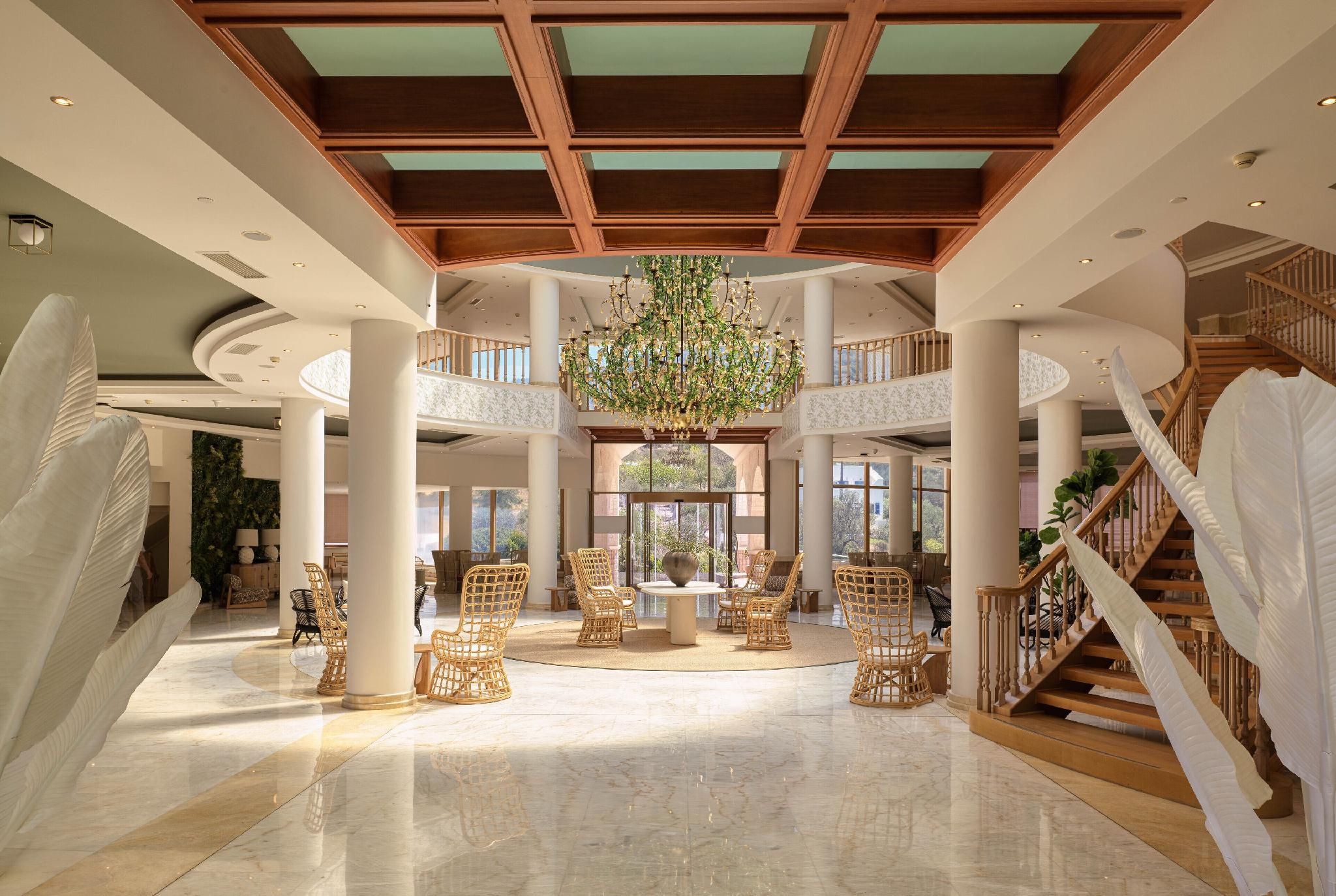 A spacious lobby with a high ceiling, a grand chandelier, and a central seating area with wicker chairs.