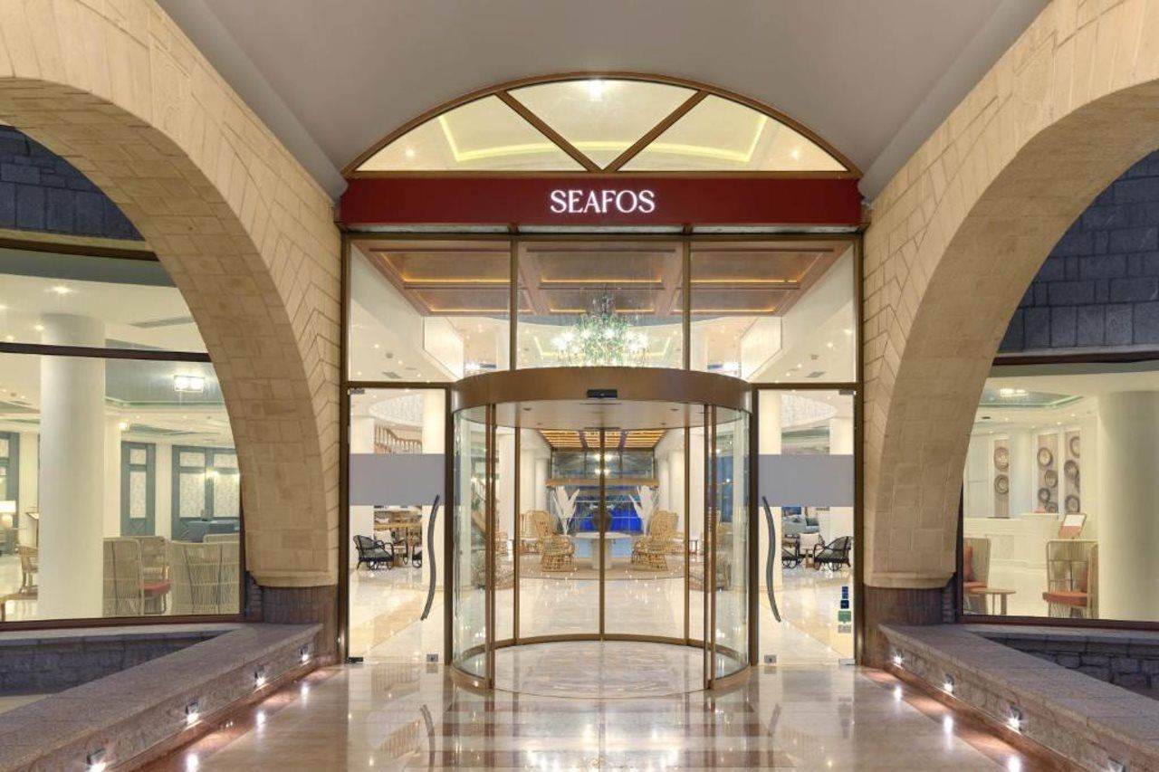 Entrada de hotel con puerta giratoria, fachada de vidrio y un letrero que dice 'SEAFOS'.