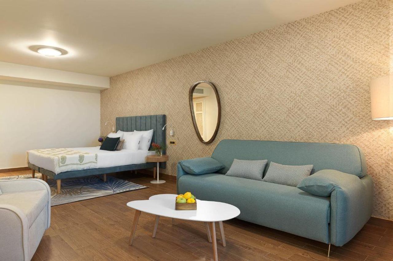 A hotel room with a bed, a sofa, a small table, and a mirror on the wall.