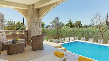 A poolside area with wicker furniture, a stone pillar, and a clear view of the surrounding landscape.