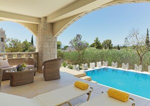 A poolside area with wicker furniture, a stone pillar, and a clear view of the surrounding landscape. - Seafos Luxury Resort & Spa (Nafplio)