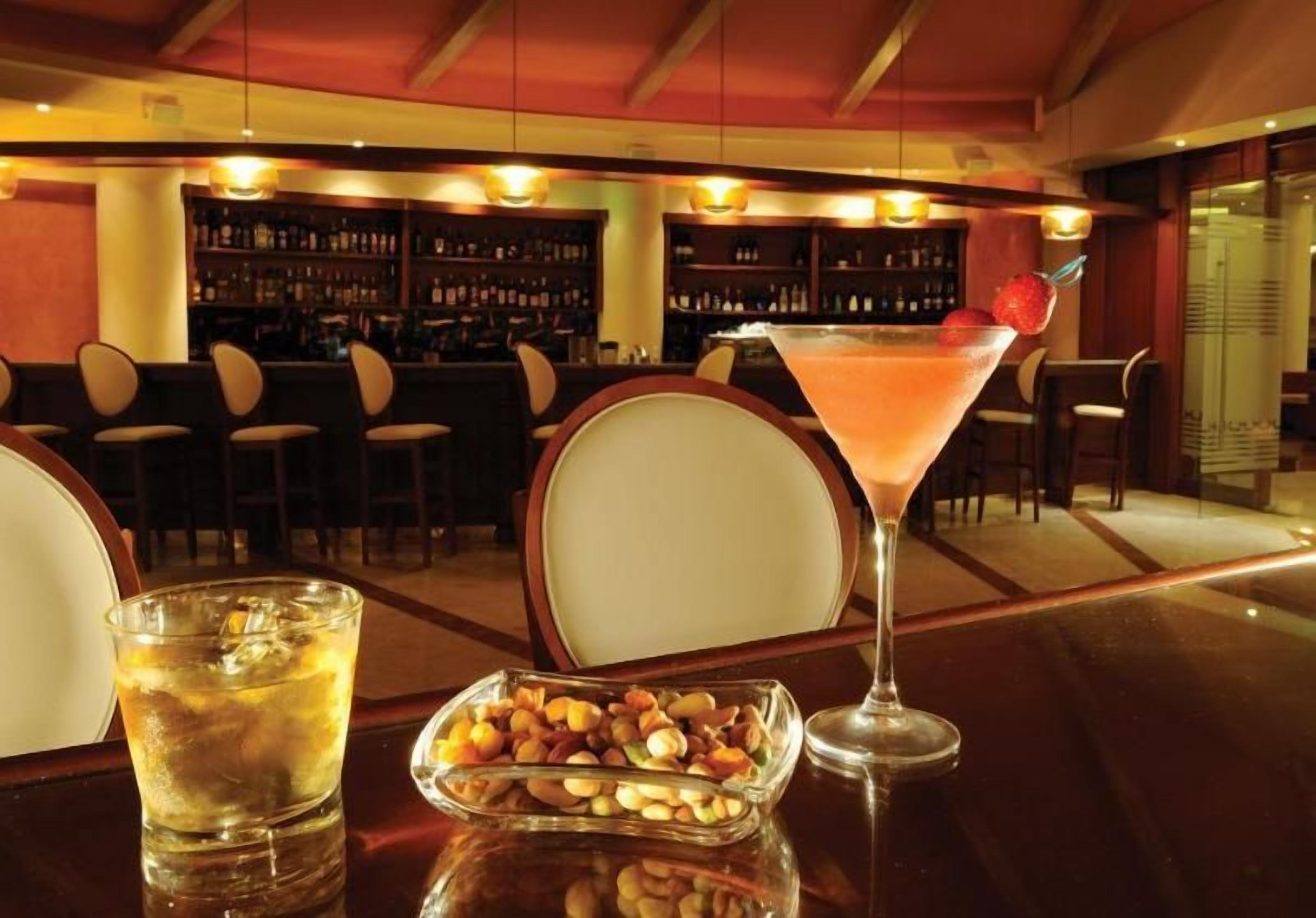 A bar area with a cocktail, a glass of beer, and a bowl of nuts on a table.