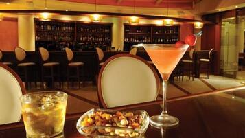 A bar area with a cocktail, a glass of beer, and a bowl of nuts on a table.