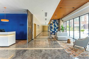 A modern reception area with a reception desk, a blue wall, a geometric patterned wall, and a large window offering a view of the outside. - Holiday Inn Express Wuxi East Station (Wuxi)