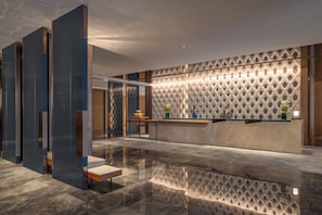 A modern reception area with a geometric patterned wall, a reception desk, and a seating area with a reflective floor. - Intercontinental Zhengzhou (Zhengzhou)