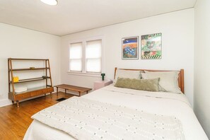 Een slaapkamer met een bed, een houten bankje, een klein tafeltje en twee kunstwerken aan de muur.