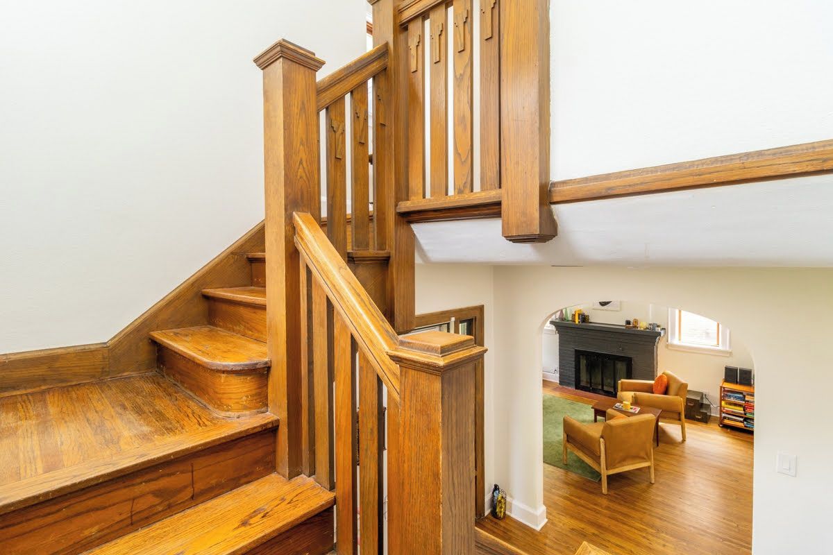 A wooden staircase leading to an upper floor, a fireplace, and a seating area with a rug and chairs.