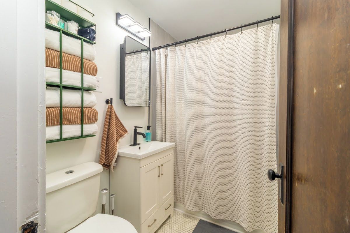 A bathroom with a toilet, sink, mirror, towel rack, and shower curtain.