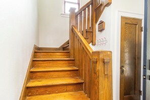 Un escalier en bois avec une rampe, une porte dotée d’une poignée en laiton et une petite fenêtre située au-dessus de la porte.
