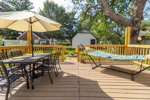 Une terrasse en bois avec une table et des chaises, un hamac et un petit abri de jardin en arrière-plan.
