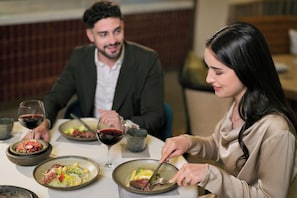 A dining table with plates of food, wine glasses, and a person cutting meat.
