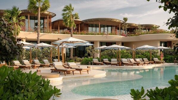 A resort pool area with sun loungers and umbrellas, surrounded by lush greenery and modern architecture.