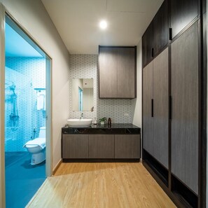 A modern bathroom with a wooden vanity, a large mirror, and a shower area visible through a glass door. - College Haus Rangnam (Bangkok)