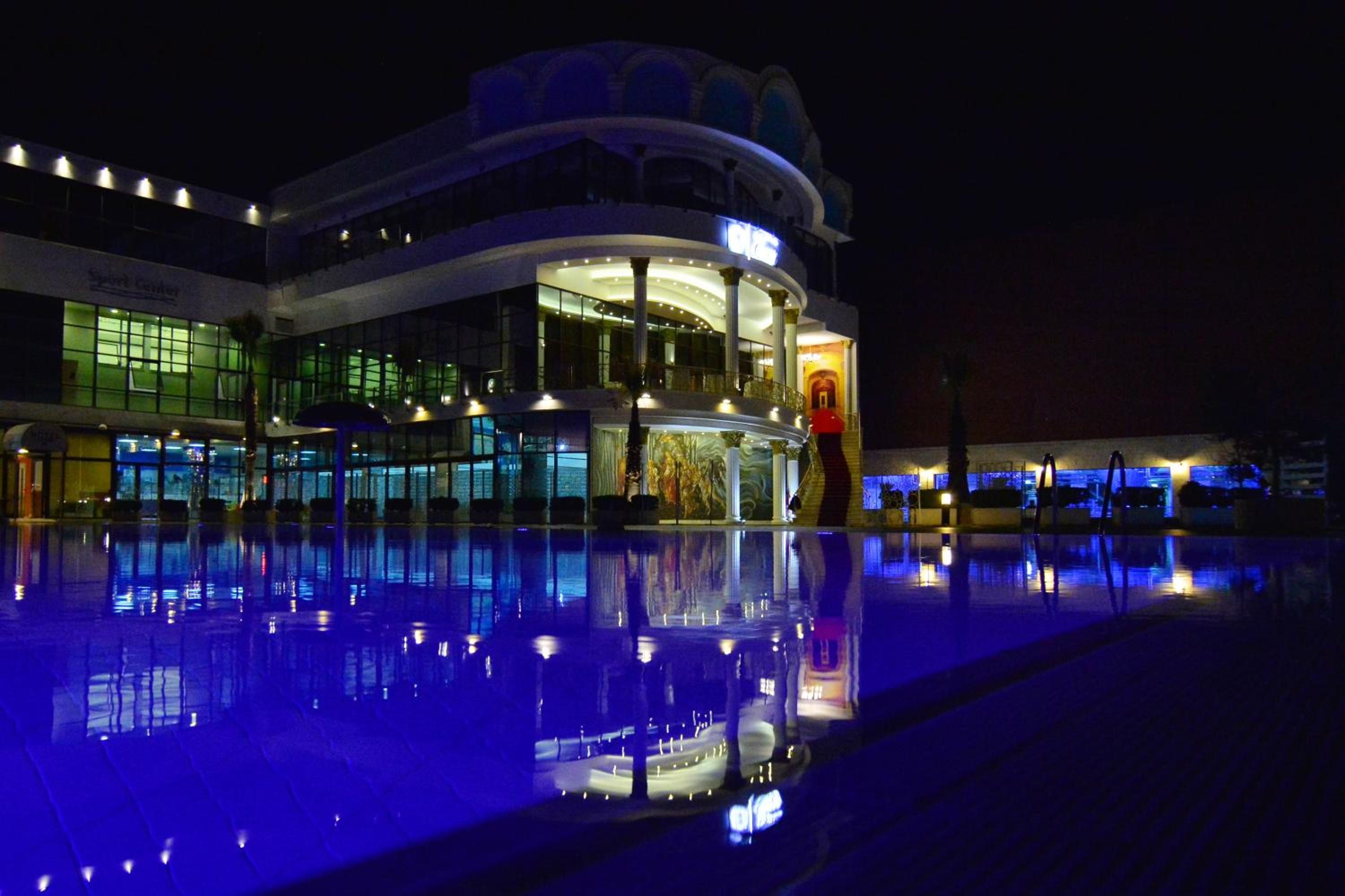 Un hotel de varios pisos con una piscina que refleja las luces del edificio.