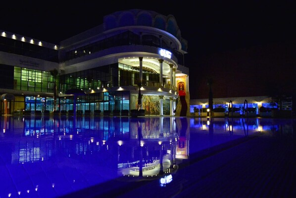 Un hotel de varios pisos con una piscina que refleja las luces del edificio.