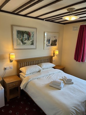 A hotel room with a bed, two bedside tables, a nightstand, a lamp, a ceiling fan, and two framed pictures on the wall. - Oakwood Bed and Breakfast Heathrow (West Drayton)